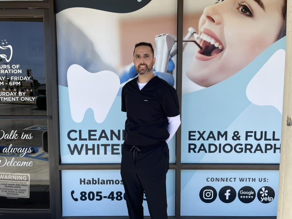 Dr. Mario Amidi outside Oxnard Dental Office on Saviers Road, in front of the window listing the practice's services.